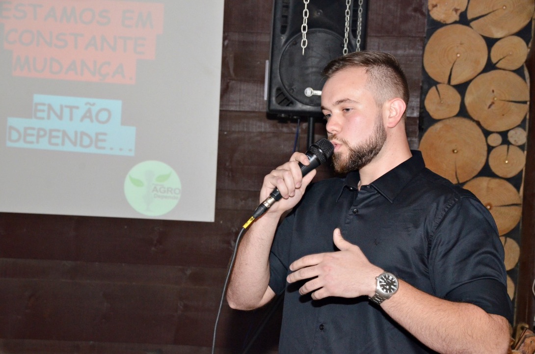 Apresentador falando ao microfone diante de um telão com o logo do Agro Depende e a frase "Estamos em constante mudança. Então depende..."